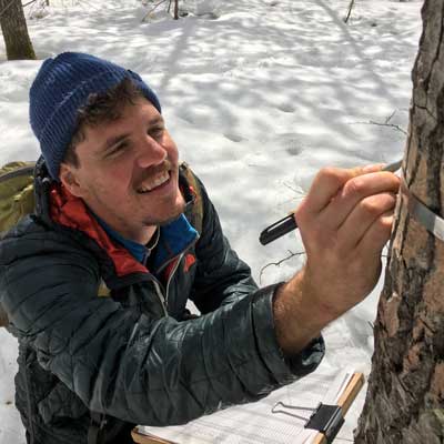 a student in the snowy woods making a mark on a tree with a sharpie