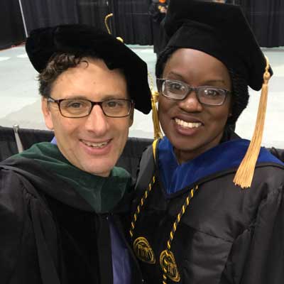 professor john ryan and a graduating student dressed in regalia at a commencement ceremony
