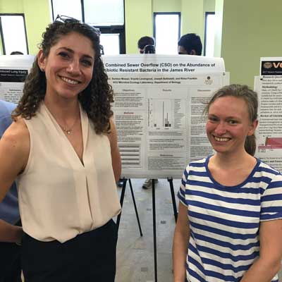 a biology professor and student stand in front of a research poster at a research conference